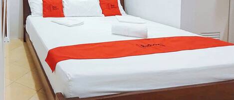 A neatly made bed with white and red bedding, a wooden headboard, and a red blanket with a logo.