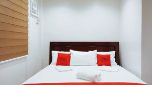 A small, neatly made bed with a white and red bedspread, two red pillows with text, and a white towel on the bed. - Reddoorz @ David's Travellers Inn Cavite (General Trias)