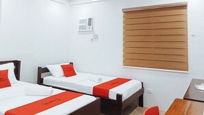 A hotel room with two single beds, a wooden desk, a chair, a window with blinds, and a wall-mounted air conditioning unit. - Reddoorz @ David's Travellers Inn Cavite (General Trias)