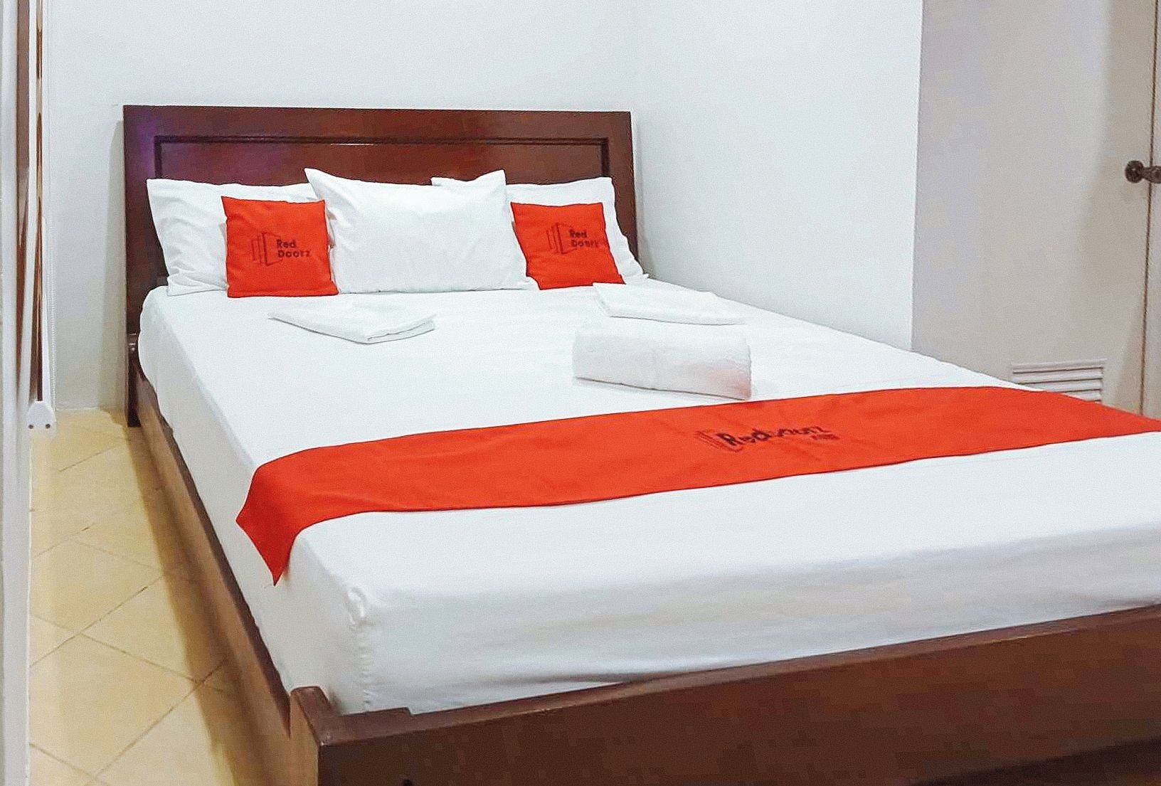 Un lit bien fait, avec une literie blanche et rouge, une tête de lit en bois et un couvre-lit rouge orné de motifs textuels.