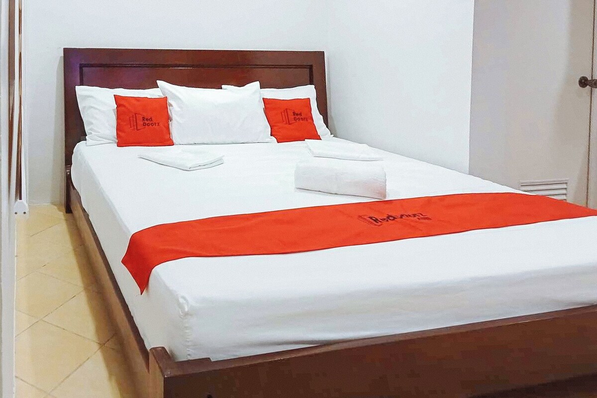 A neatly made bed with white and red bedding, a wooden headboard, and a red bed runner with text.