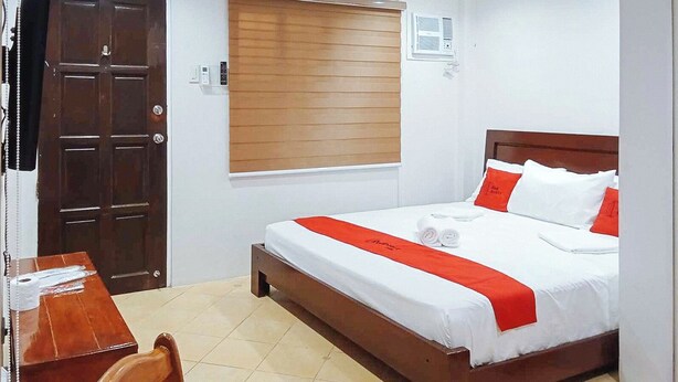 A hotel room with a wooden bed, white bedding, a red accent, a wooden desk, and a chair. - Reddoorz @ David's Travellers Inn Cavite (General Trias)