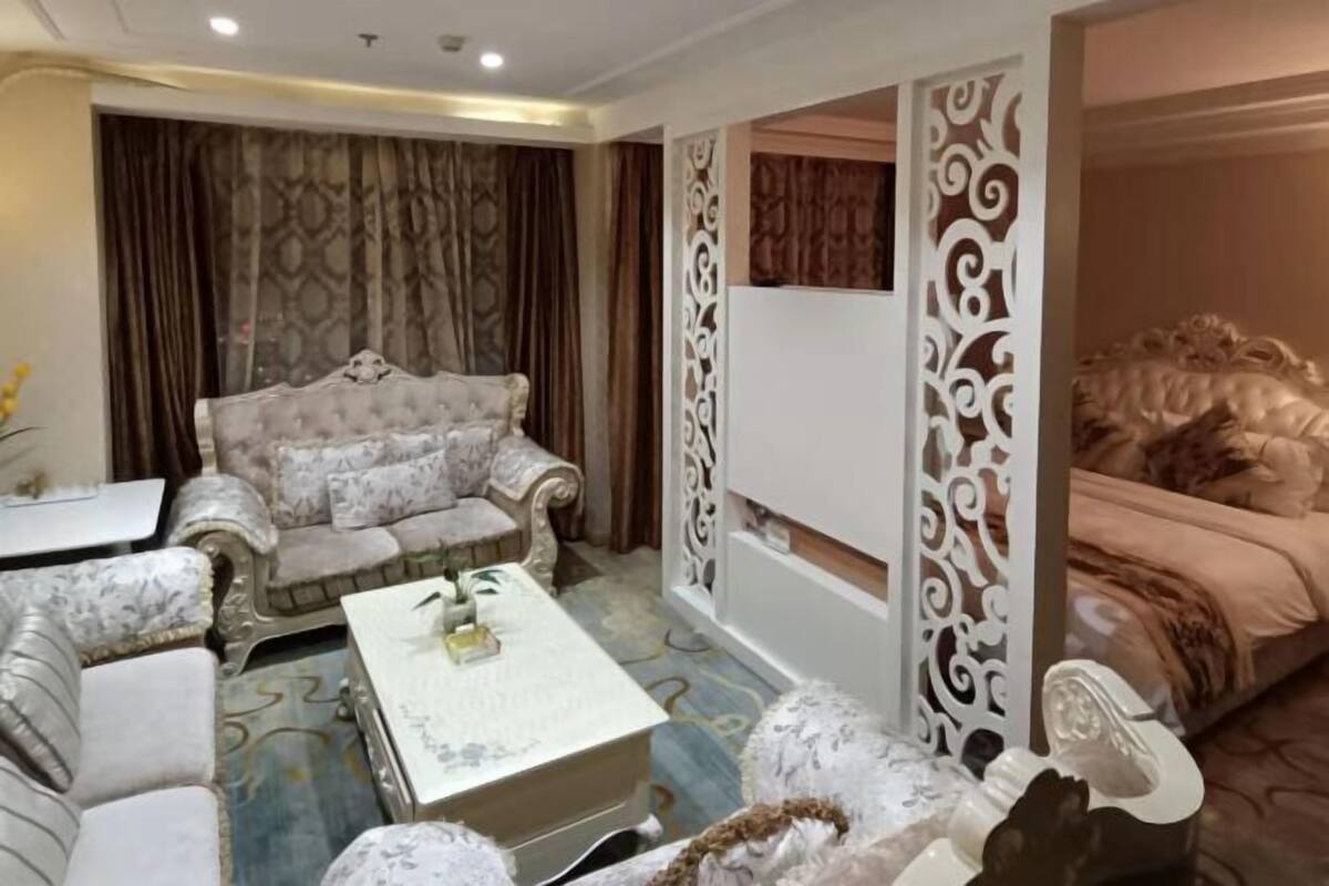 Une chambre d’hôtel comprenant un grand canapé, un fauteuil plus petit, une table basse et un lit doté d’une tête de lit décorative.