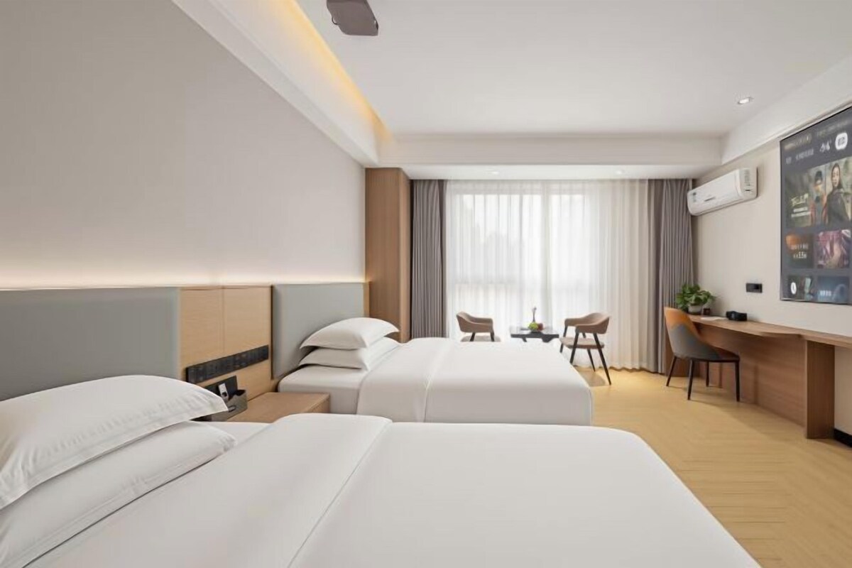 A hotel room with two beds, a desk, a chair, and a TV.