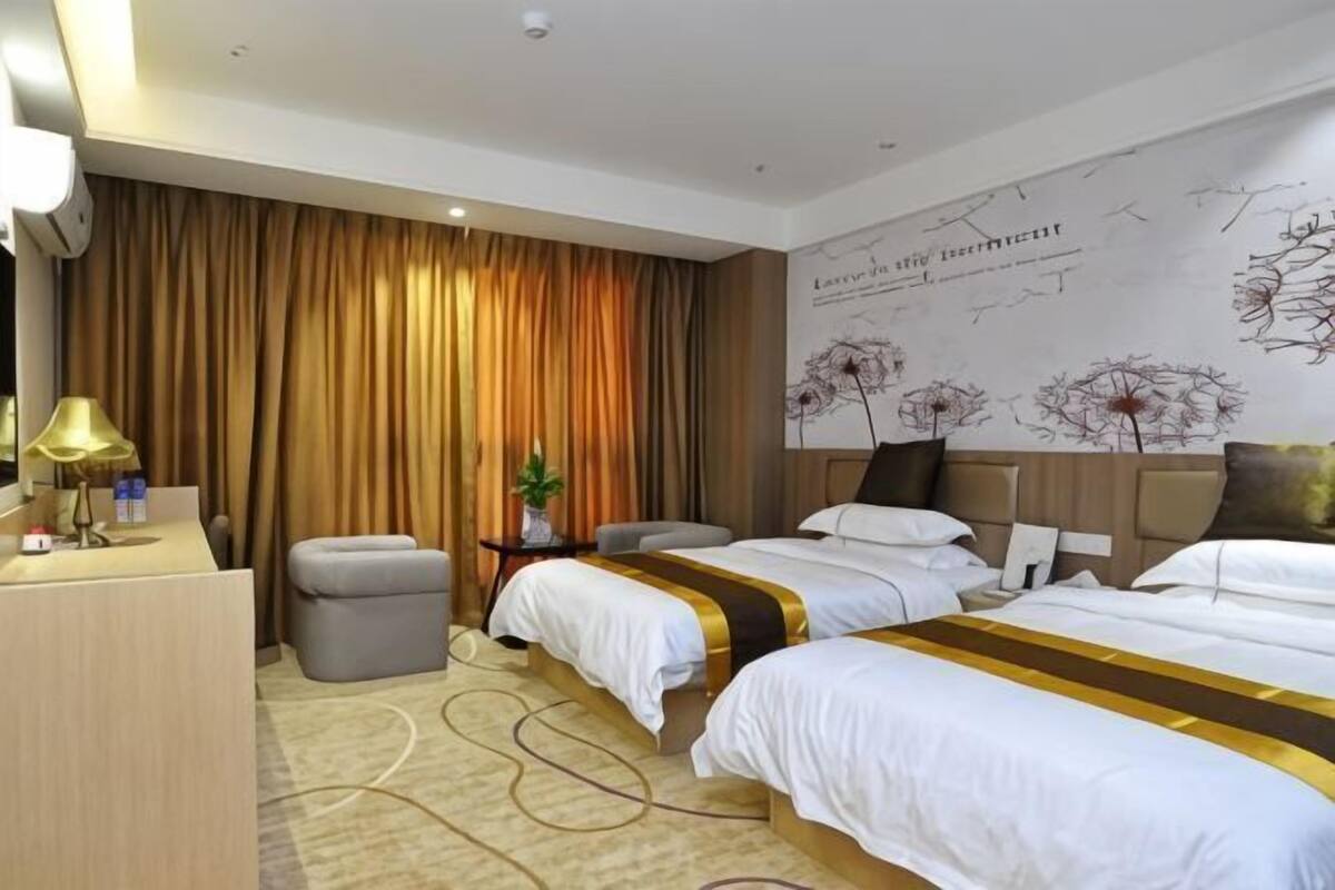 Une chambre d’hôtel avec deux lits, un bureau, une chaise, une petite table avec une lampe et une grande fenêtre avec des rideaux.