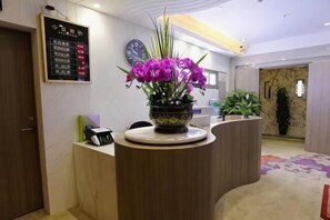 Un comptoir d’accueil orné d’un vase de fleurs violettes, d’une horloge et d’un panneau d’affichage numérique.