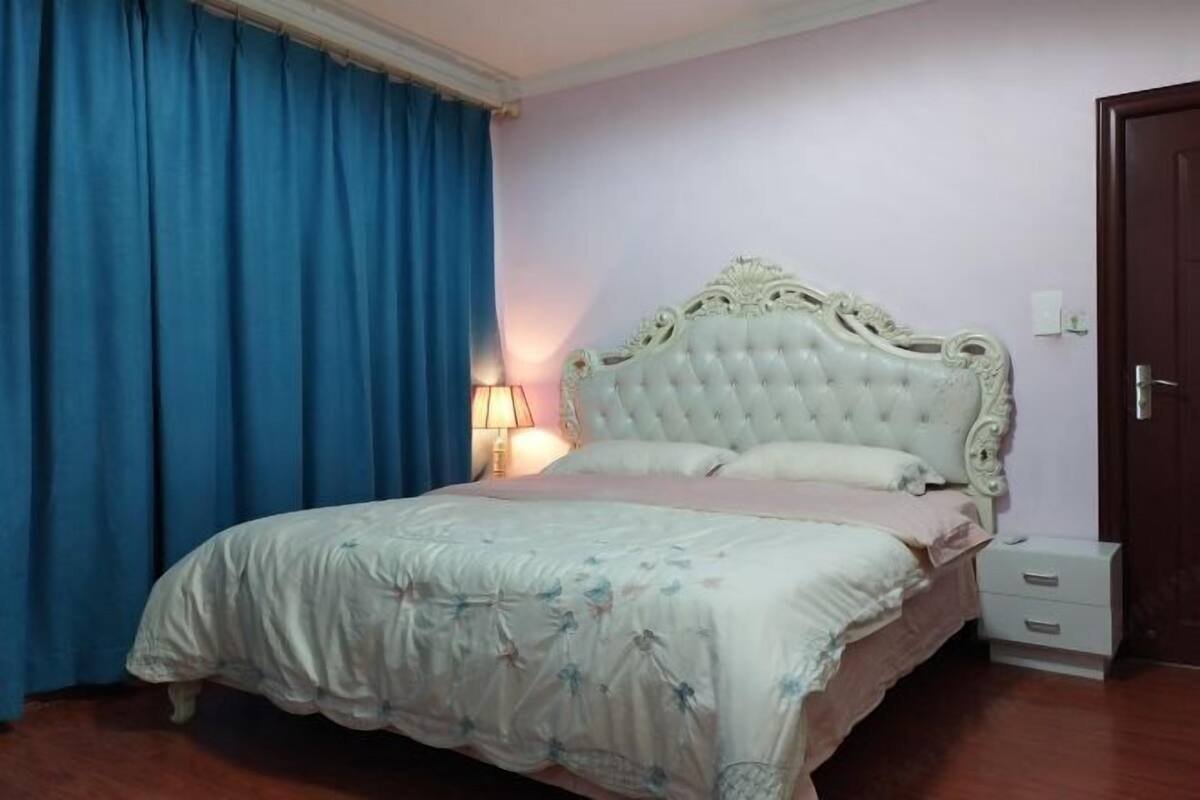 Une chambre à coucher avec un grand lit, une table de chevet, une lampe et une porte.