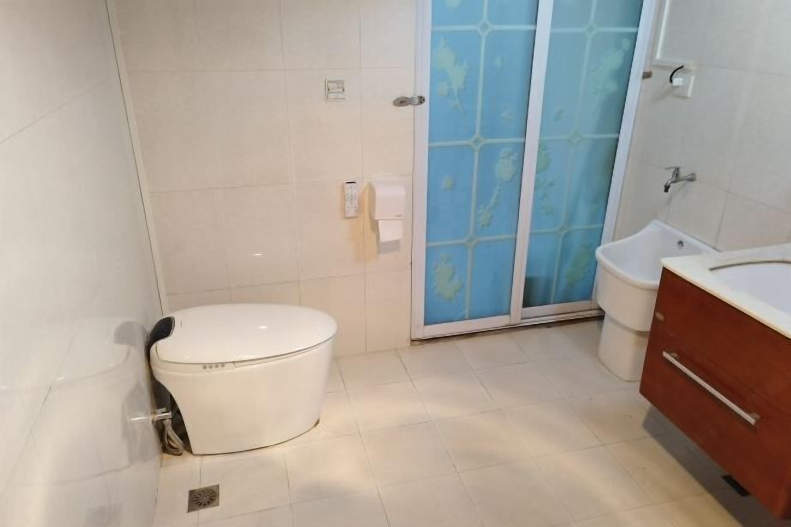 A bathroom with a toilet, a shower with a glass door, and a sink with a wooden cabinet.
