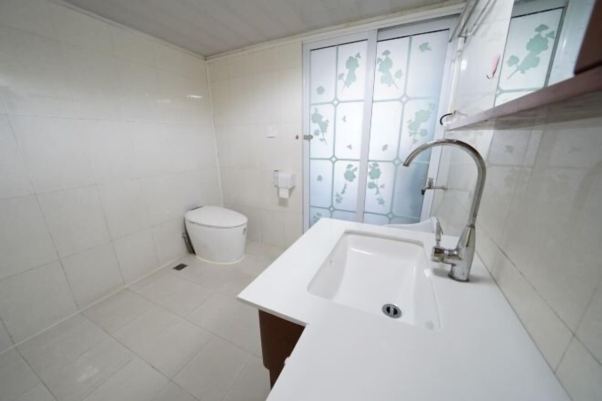 Een badkamer met witte tegels, een witte wastafel, een toilet en een raam met geëtste ruit.