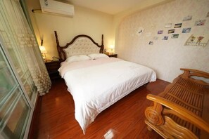 Een slaapkamer met een houten bed, een nachtkastje, een houten stoel en een wand met foto's.