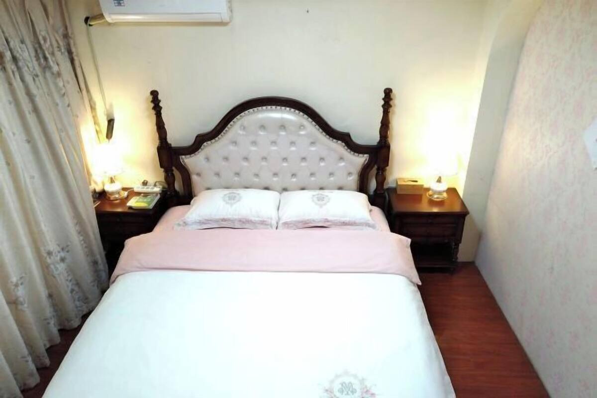 Una cama individual con cabecera de madera, dos mesitas de noche con lámparas y una colcha de estampado floral.