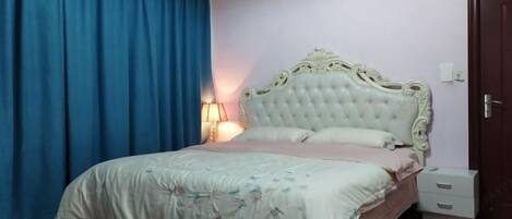 A bedroom with a large bed, a nightstand, a lamp, and a door.