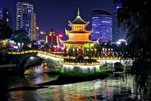 A traditional building with a prominent roof, situated by a water body, with a bridge in the foreground.