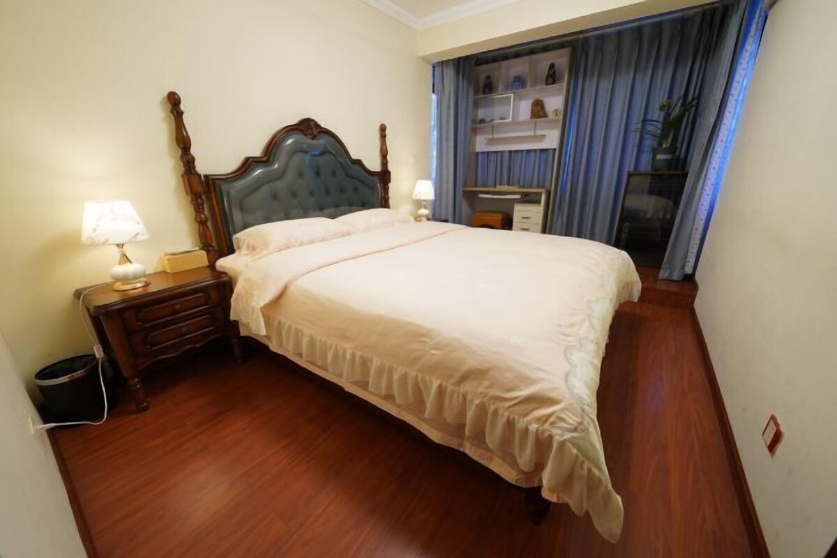 Een hotelkamer met een groot bed, een houten hoofdbord, nachtkastjes met lampen, een dressoir en een bureau met stoel.
