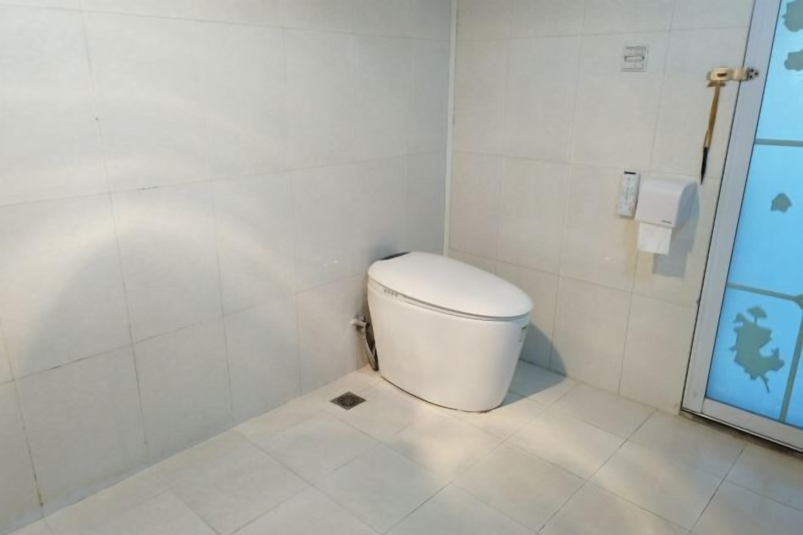 A small, white toilet in a corner of a room with white tiled walls and floor.