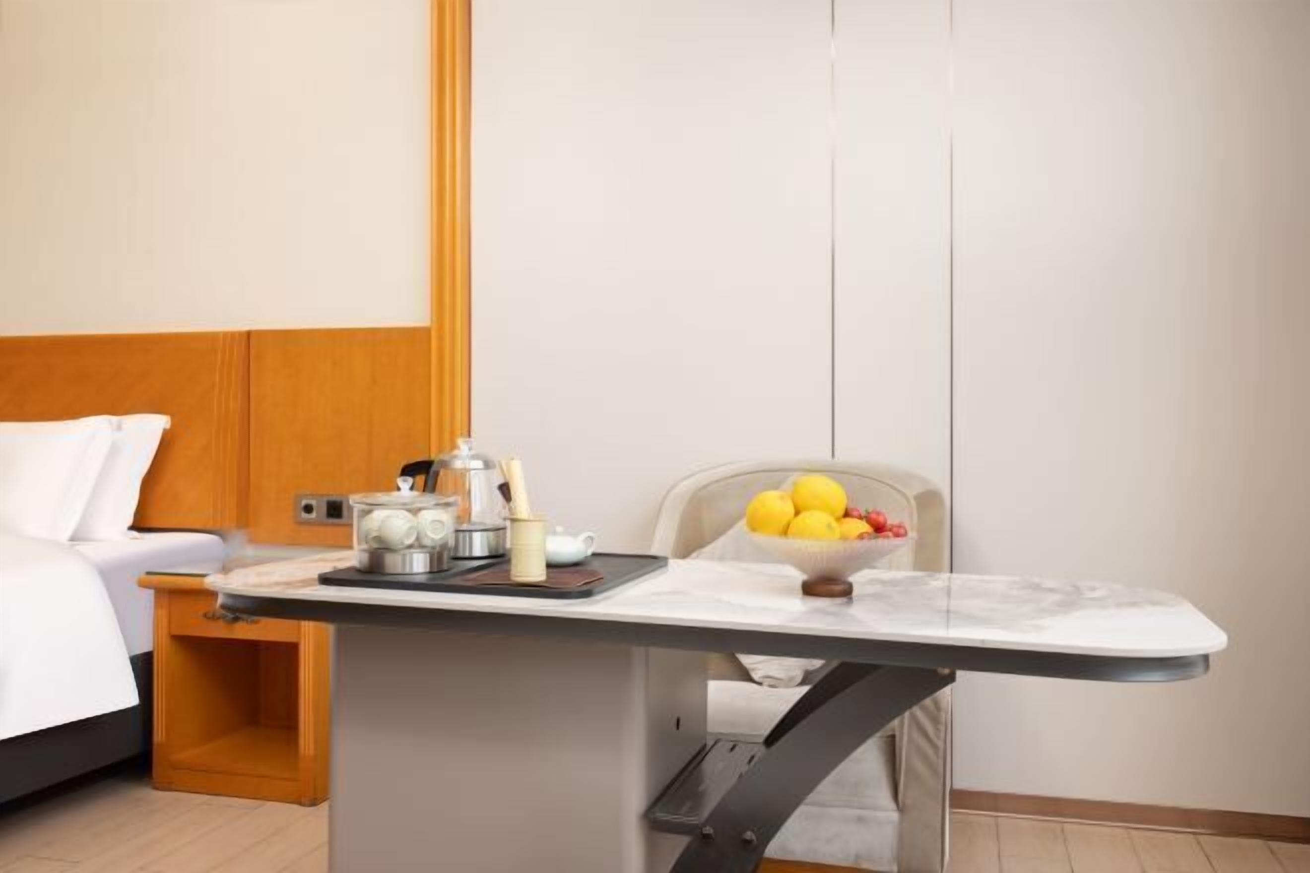 Ein kleines Hotelzimmer mit Bett, einem Tisch mit Obstschale, einem Wasserkocher und einer Tasse.