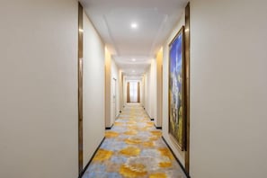 Un pasillo de hotel con alfombra estampada, obras de arte enmarcadas en las paredes y una lámpara en el techo.