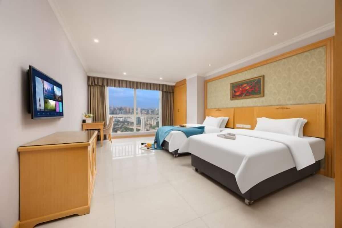 Ein Hotelzimmer mit Bett, Schreibtisch, Sessel, Fernseher und einem großen Fenster mit Blick auf die Stadt.