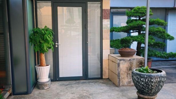 Entrada de un edificio con puerta corredera de vidrio, una planta en maceta y un bonsái.