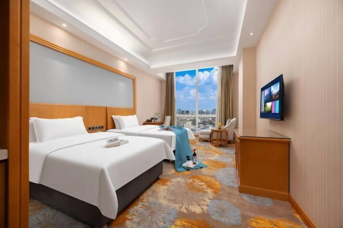 Ein Hotelzimmer mit zwei Betten, einem Fernseher, einem Schreibtisch und Blick auf die Stadt.