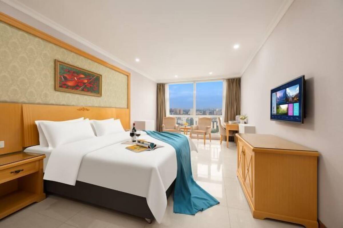 Ein Hotelzimmer mit Bett, Schreibtisch, Fernseher und Blick auf die Stadt.