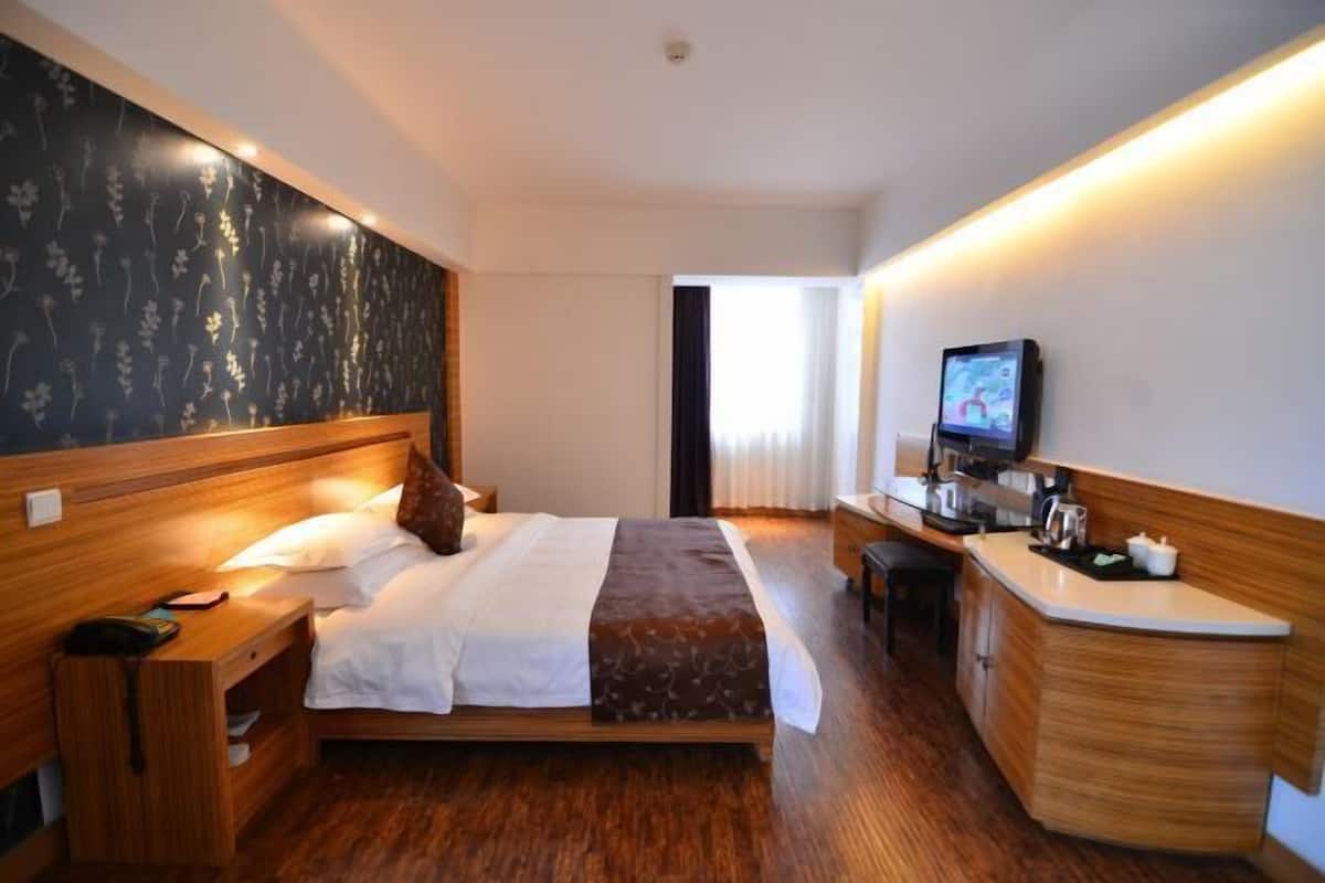 A hotel room with a wooden bed, a small bedside table, a TV, and a kitchenette area.