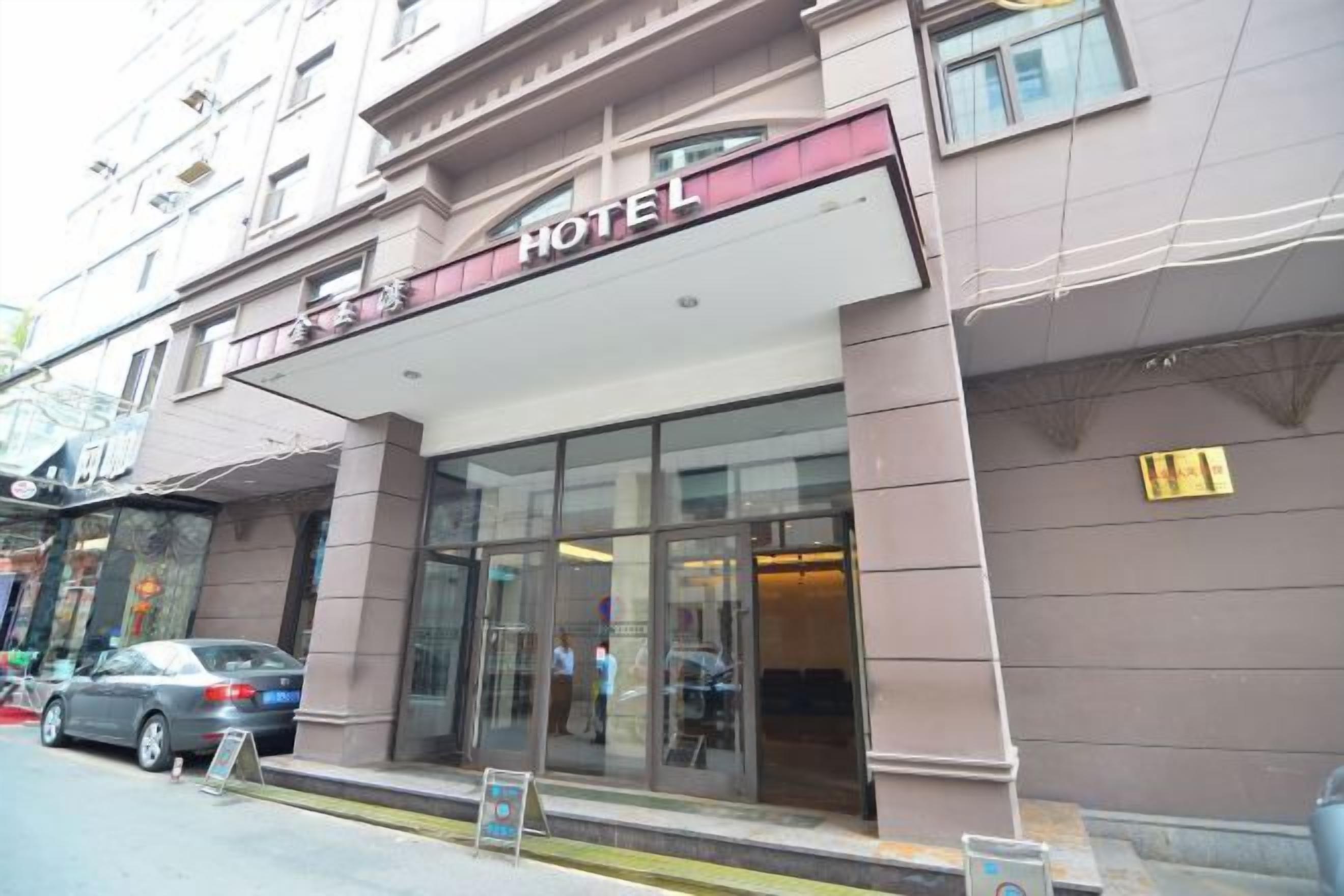 Entrada de un hotel con fachada de vidrio, un letrero sobre la entrada y un coche estacionado afuera.