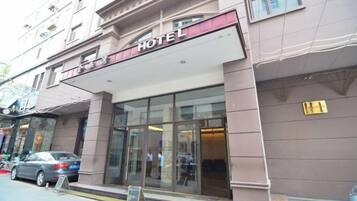 Entrada de un hotel con fachada de vidrio, un letrero sobre la entrada y un coche estacionado afuera.