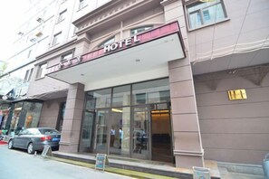 A hotel entrance with a glass facade, a sign above the entrance, and a car parked outside. - Jinyuwan Hotel (Dalian)