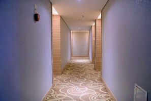 A hotel hallway with patterned carpet, wooden paneling on the walls, and a light fixture on the ceiling. - Jinyuwan Hotel (Dalian)
