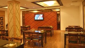 A dining area with multiple tables and chairs, a television screen on the back wall, and a decorative column. - Jinyuwan Hotel (Dalian)