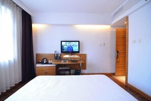A hotel room with a bed, a desk with a TV, a wooden wardrobe, and a door. - Jinyuwan Hotel (Dalian)