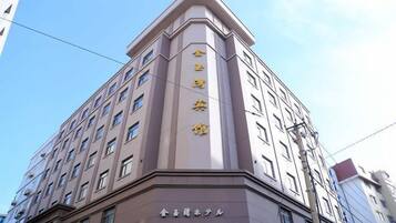 Un hotel de varios pisos con una entrada destacada en esquina, un letrero que indica que es un hotel y un cielo despejado al fondo.