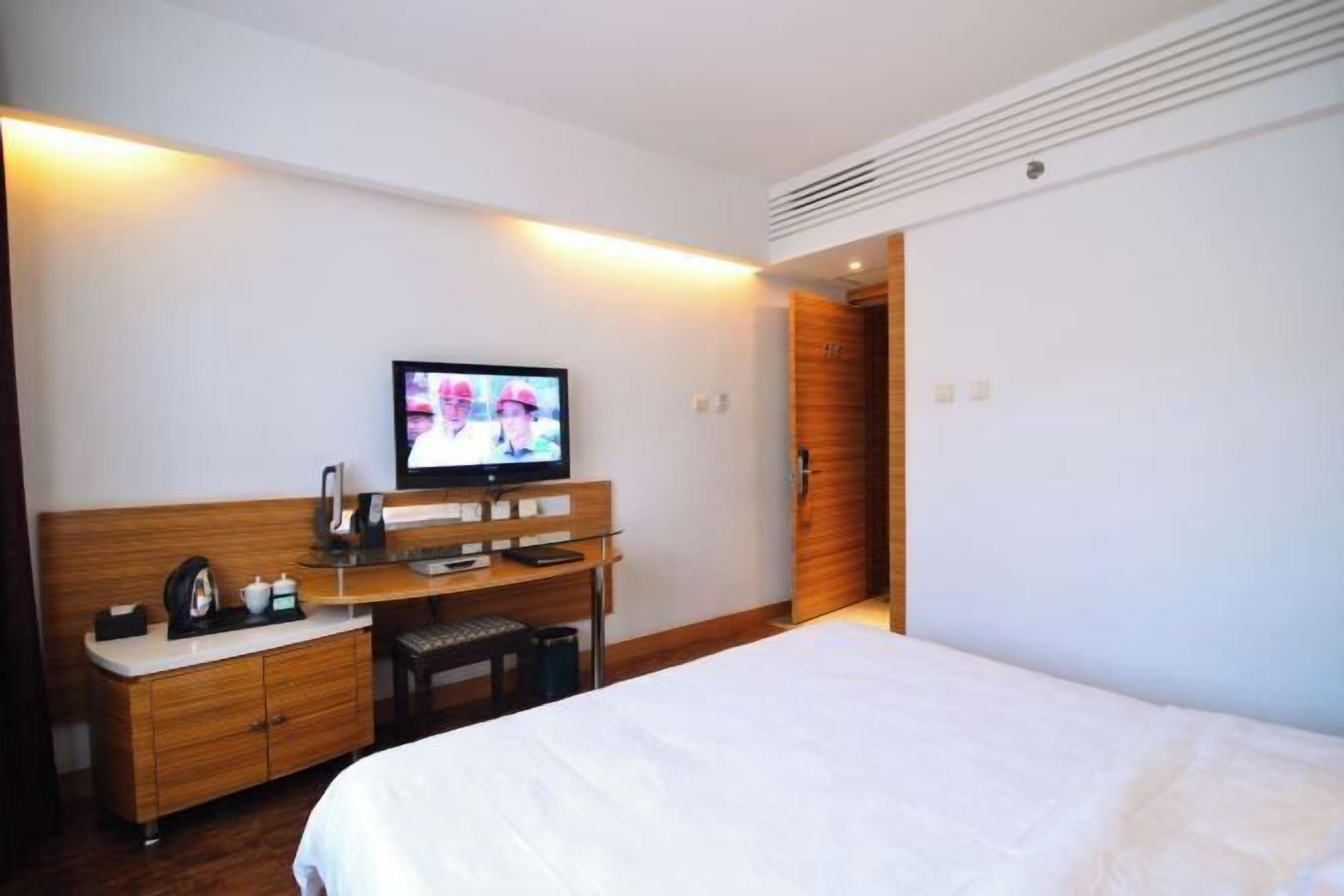 Una habitación de hotel con una cama, un escritorio con televisor y un armario de madera.