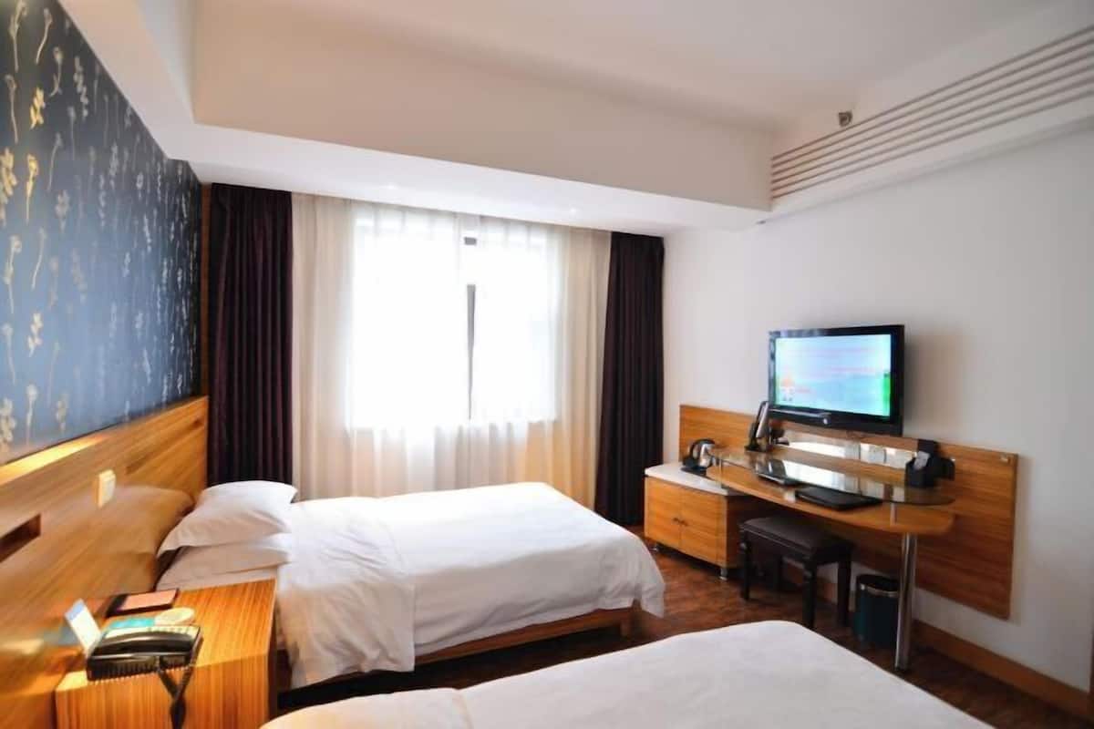 A hotel room with two beds, a desk with a computer and a television, and a large window with curtains.