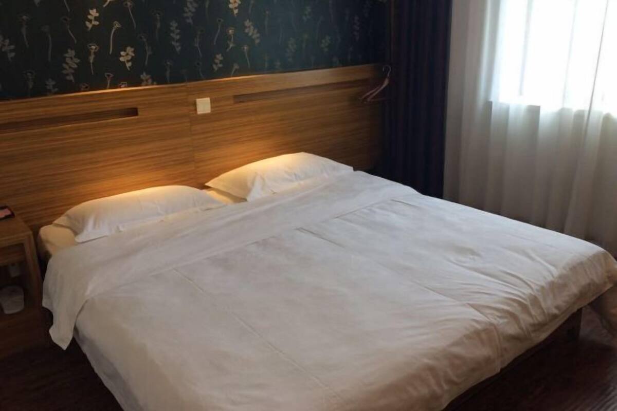 A neatly made bed with white linens in a room with floral wallpaper and a wooden headboard.