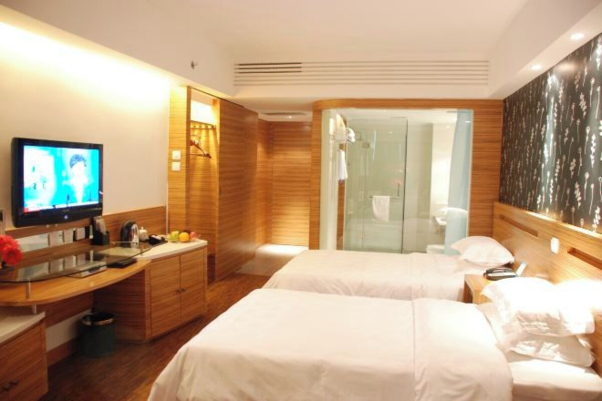 Habitación de hotel con dos camas, televisor, tocador de madera y zona de ducha.