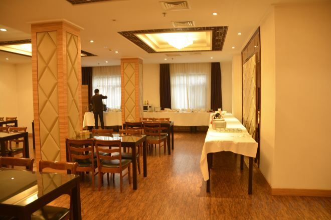 A hotel dining area with tables and chairs, a person standing near the counter, and a view of the room.