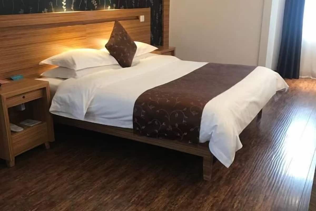 A neatly made bed with white and brown linens, a wooden headboard, and a nightstand with a lamp.