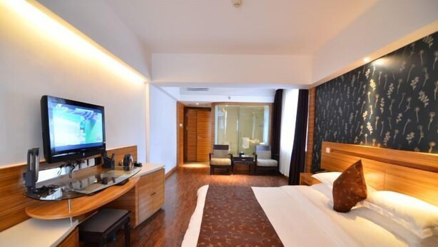 A hotel room with a bed, a desk with a television, a small table, and a chair. - Jinyuwan Hotel (Dalian)