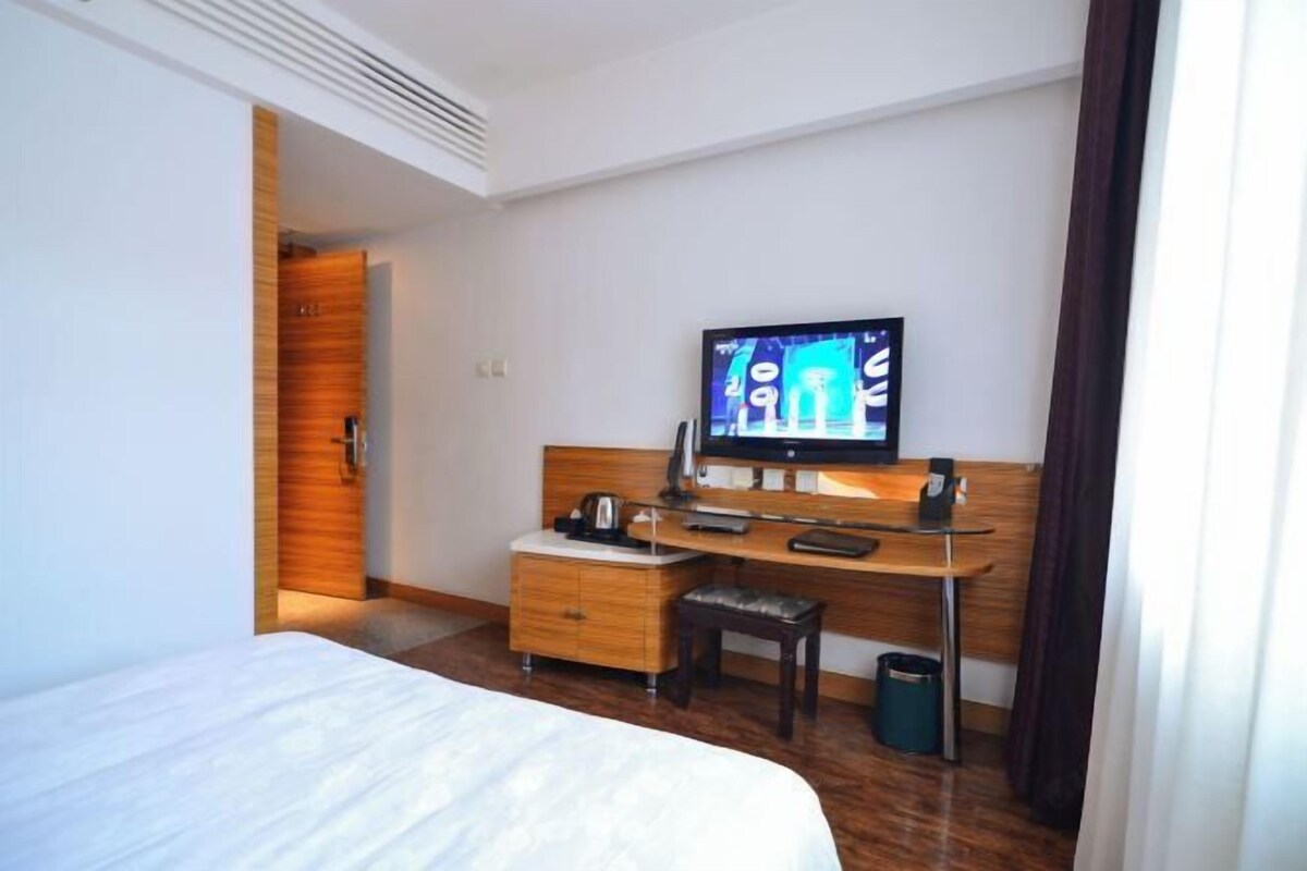 A hotel room with a bed, a desk with a computer, a small table, and a chair.