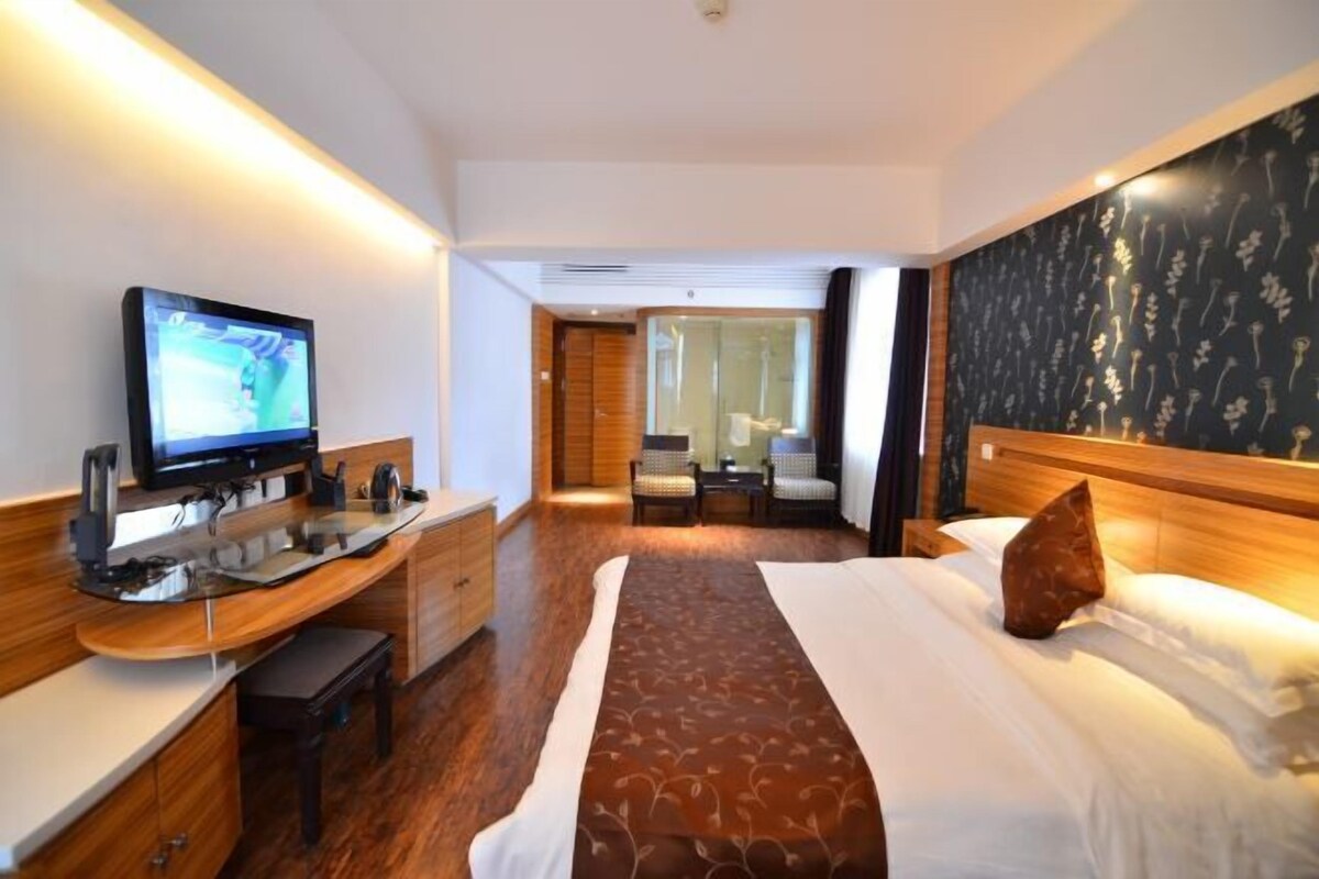 A hotel room with a bed, a desk with a computer, a television, and a view of the hallway.