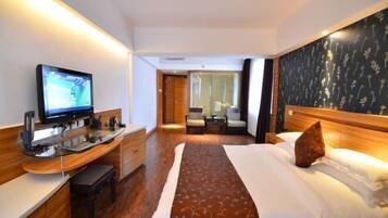 A hotel room with a bed, a desk with a computer, a television, and a view of the hallway.