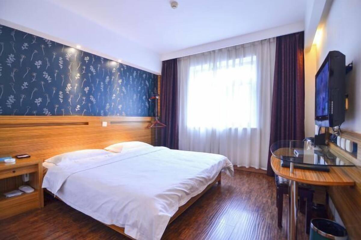 A hotel room with a wooden bed, a small bedside table, a TV, and a window with curtains.