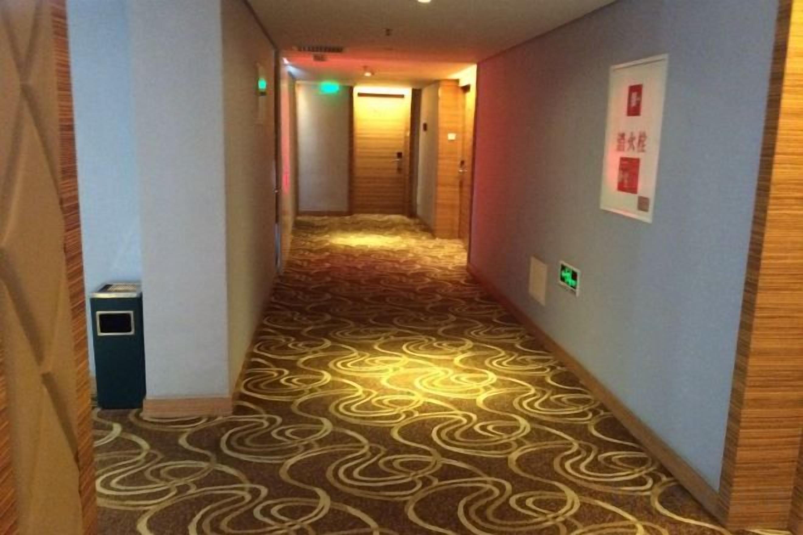 Ein Hotelgang mit gemustertem Teppich, einem Mülleimer und Notausgangsschildern.