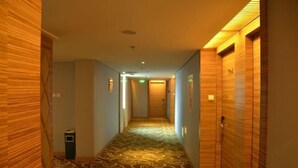A hotel hallway with patterned carpet, wooden walls, and a trash bin. - Jinyuwan Hotel (Dalian)