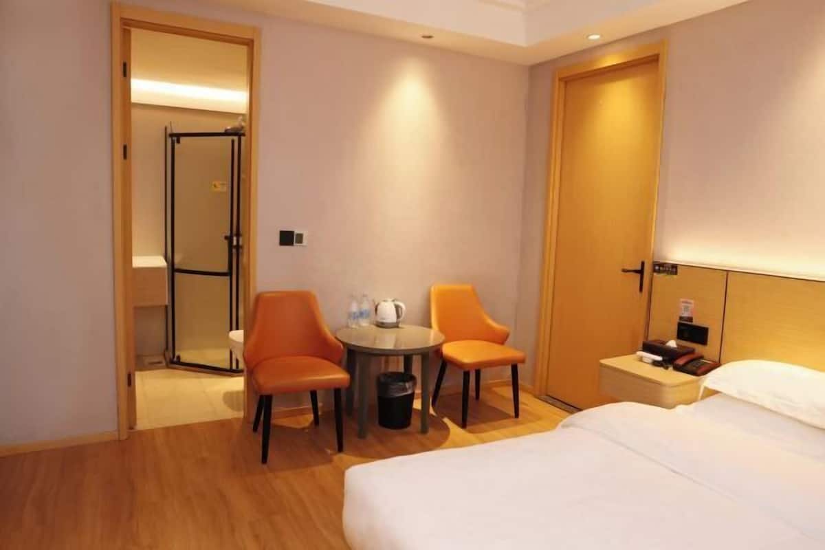 A hotel room with a bed, a small table with two chairs, a nightstand, and a door leading to a shower area.
