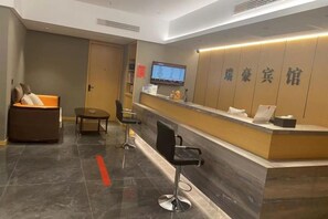 A hotel reception area with a reception desk, seating, and a television screen. - Ruihao Hotel (Pingyang)