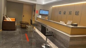 A reception area with a reception desk, a seating area with a sofa and chairs, a television screen, and a wall with Chinese characters. - Ruihao Hotel (Pingyang)