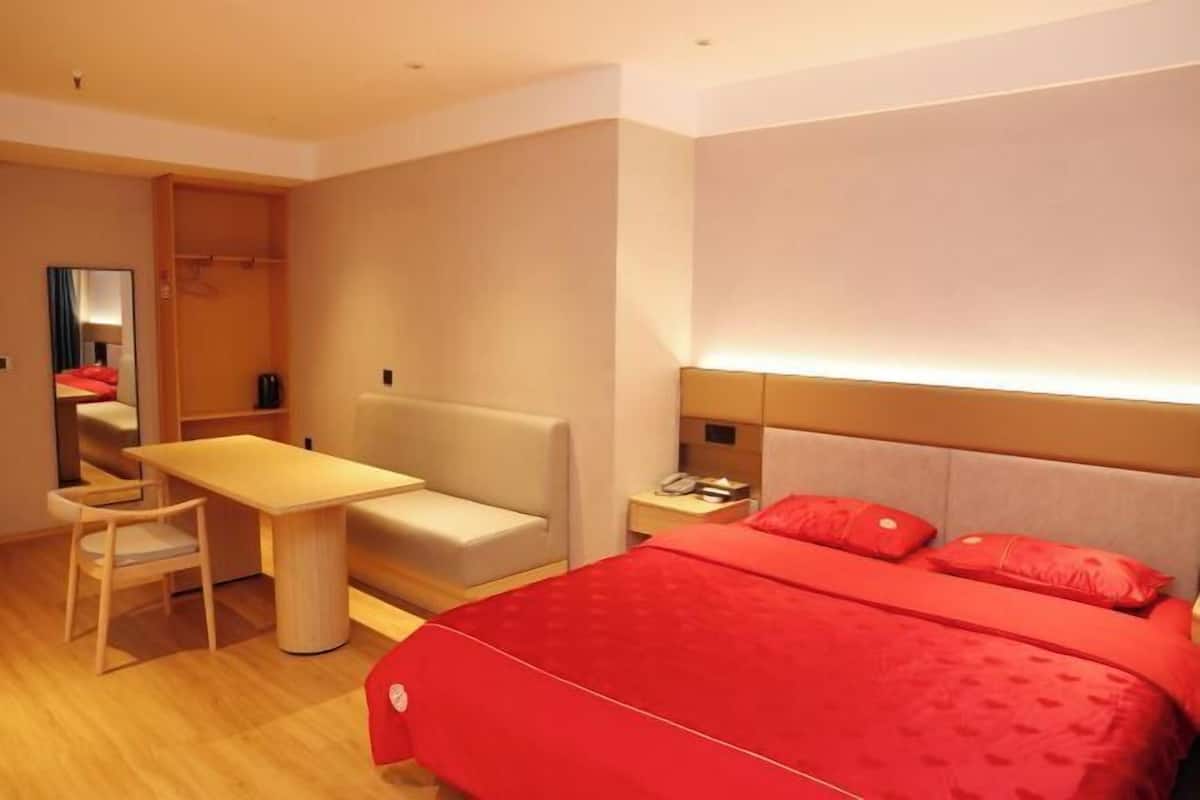 A modern hotel room with a large bed, a desk, a chair, and a wardrobe.